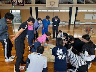 女性消防団員の胸骨圧迫を救命講習受講者が輪になって見ている写真