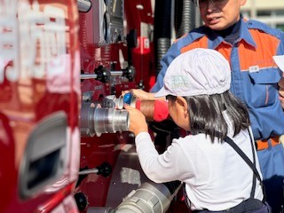 こどもが消防車両にホースをつないでいる写真