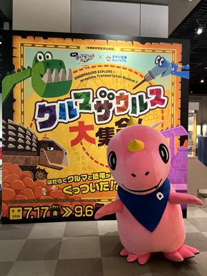大きなポスターの前でポーズをとるあみゴン