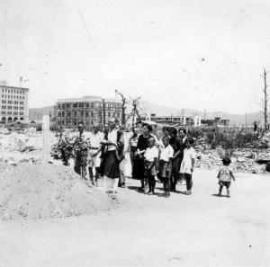 被爆した町の中に建てられた供養塔と供養する僧と人々の写真